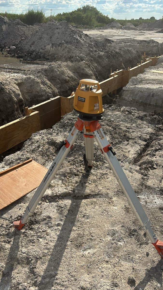 Rotary laser level on tripod over a foundation trench at the Block Forever project