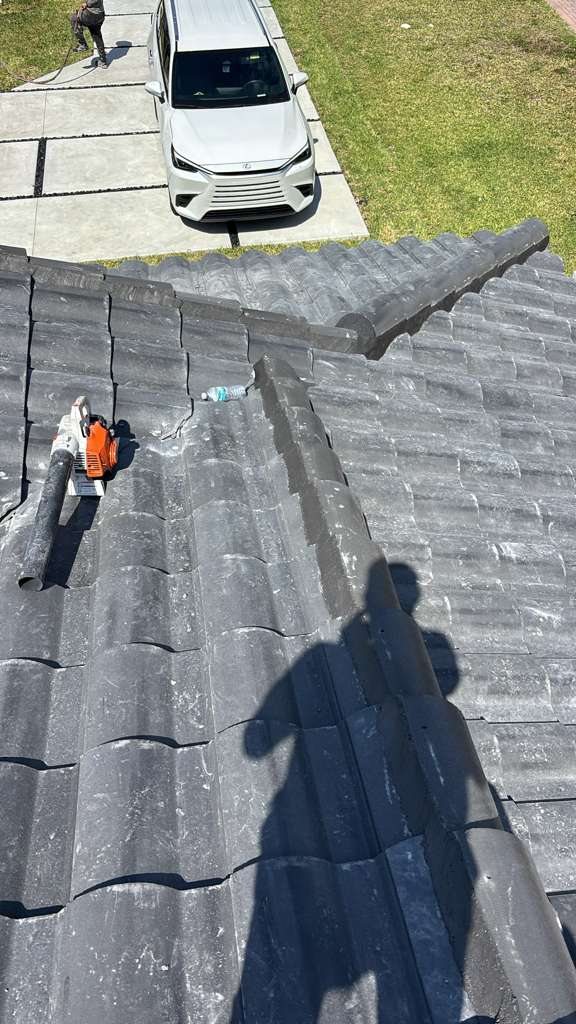 Roof crew finishing a gray tile installation with cleanup tools next to a Lexus SUV in the driveway